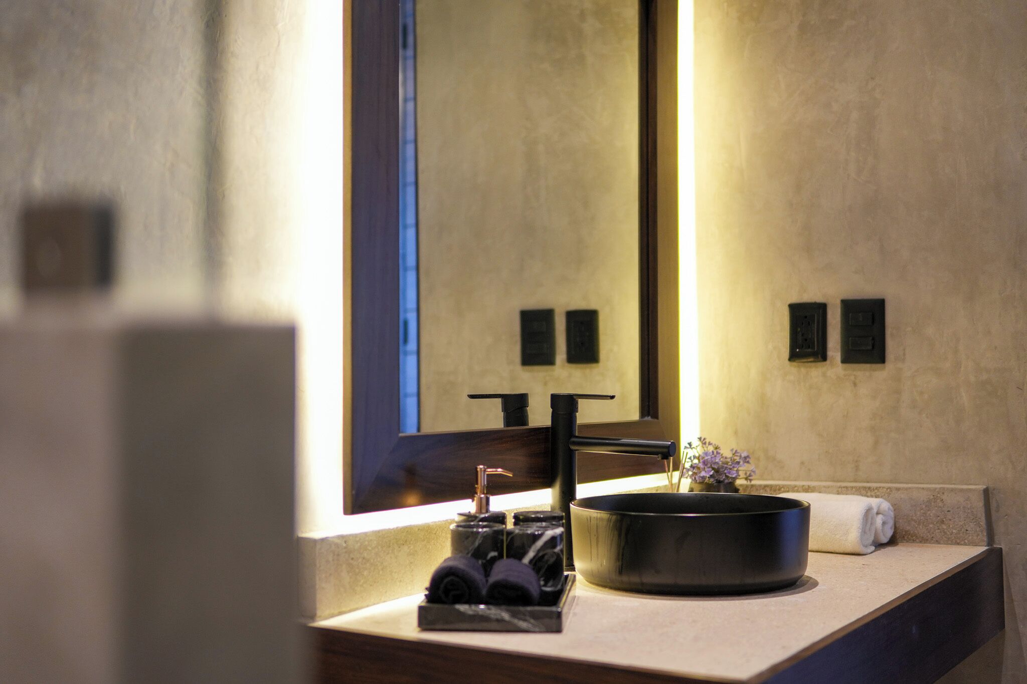 A bathroom with a large mirror, a black sink, and a towel on the counter.