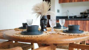 A round wooden dining table with a woven placemat, black and blue dinnerware, and a decorative vase with pampas grass. - Elegant Studio in Holistika: Your Tulum Sanctuary (Tulum)