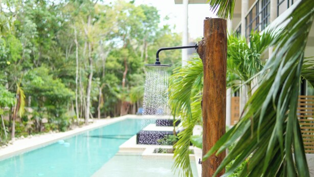 A pool with a waterfall feature surrounded by lush greenery. - Elegant Studio in Holistika: Your Tulum Sanctuary (Tulum)