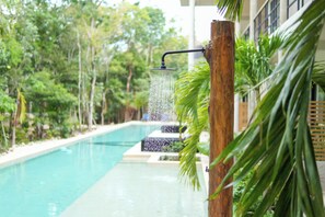 A pool with a waterfall feature surrounded by lush greenery. - Elegant Studio in Holistika: Your Tulum Sanctuary (Tulum)