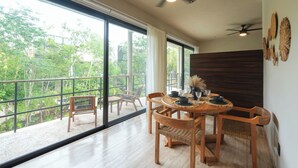 A dining area with a round table, chairs, and a view of greenery through large windows. - Elegant Studio in Holistika: Your Tulum Sanctuary (Tulum)