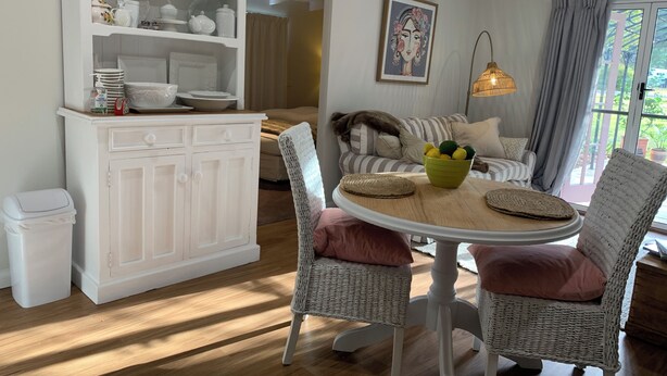 Un coin repas avec des chaises en osier, une table ronde et un buffet blanc contenant de l’ustensile de cuisine.