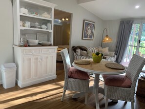 A dining area with wicker chairs, a round table, and a white cabinet with kitchenware. - Nestled at the Base of Toowoomba Range …A beautiful comfortable rural cottage . (Helidon Spa)