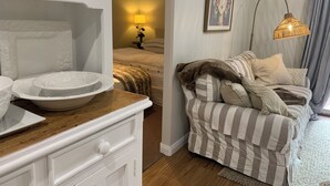 Une chambre d’hôtel chaleureuse, avec une commode en bois, un lit recouvert d’une literie à rayures, un tableau au mur et une lampe sur pied.