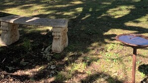 Un patio couvert aménagé avec du mobilier d’extérieur, un banc en pierre et un abreuvoir à oiseaux.