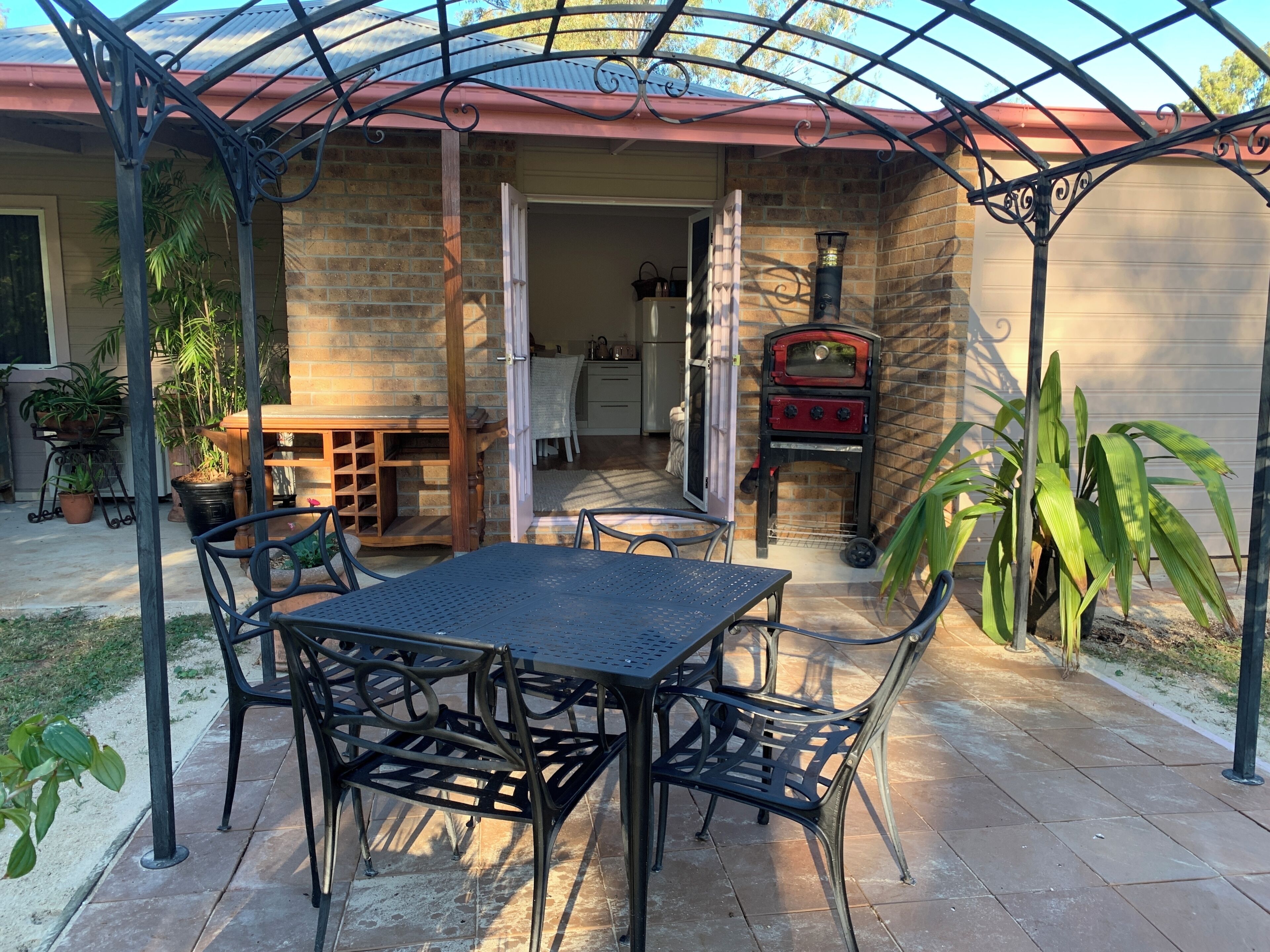 Un patio al aire libre con una mesa y sillas de metal, un muro de ladrillo y una parrilla roja.