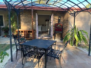 Un patio al aire libre con una mesa y sillas de metal, un muro de ladrillo y una parrilla roja.