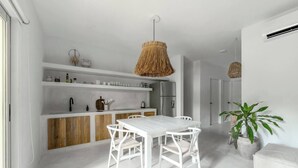 Una cucina moderna con mobili bianchi, una parete d'accento in legno e un'area pranzo con tavolo e sedie bianche.