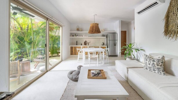 Un soggiorno moderno con un divano bianco, un tavolo da pranzo con sedie, un tavolino e una zona cucina con frigorifero e scaffali.