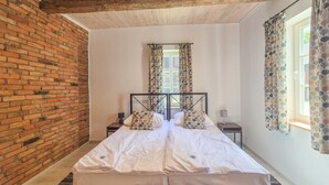 Uma cama de casal com estrutura de metal, duas mesas de cabeceira e uma janela com cortinas estampadas.