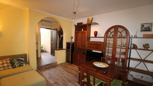 A cozy living room with a sofa, a dining table with chairs, a wooden cabinet, and a decorative shelf.