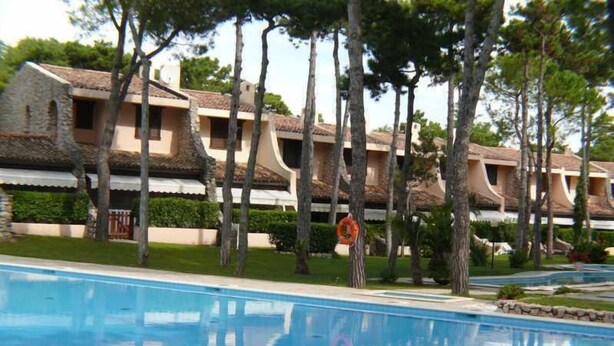 A swimming pool with a reflection of trees and a building with multiple balconies.