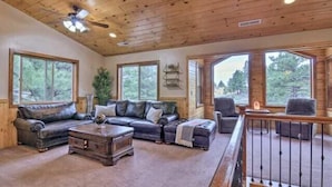 A spacious living room with a wooden ceiling, large windows, a leather sofa, a coffee table, and a staircase. - Bridgeway House (Duck Creek Village)