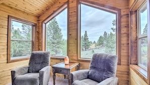 A cozy cabin room with wooden walls and large windows offering a forest view. - Bridgeway House (Duck Creek Village)