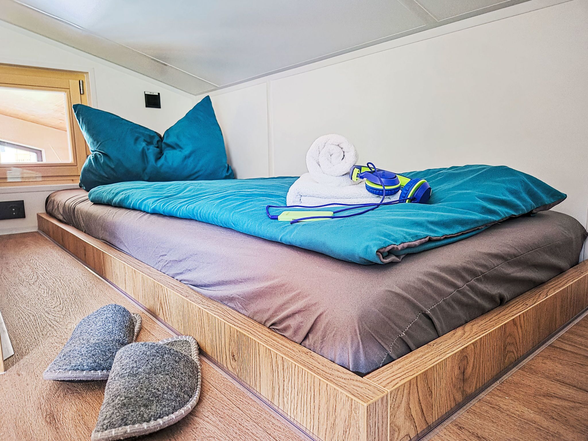 A bed with blue and brown bedding, a rolled towel, and headphones.