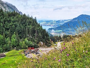 A mountainous landscape with a red bus, a parking area, and a building with a sloped roof.