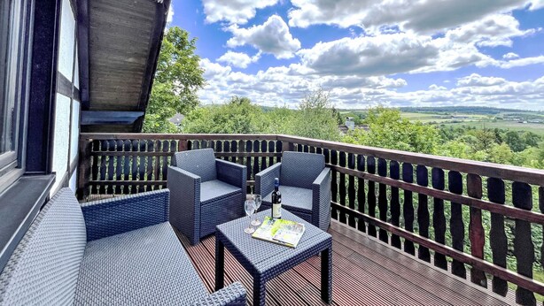 A balcony with wicker furniture and a table, overlooking a scenic landscape.