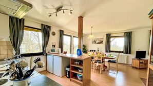 A compact kitchen with a microwave, kettle, and kettle on the counter. There is a dining area with a table and chairs, and a TV in the corner.