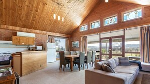 A spacious living area with a wooden ceiling, a dining table with chairs, a sofa, and large windows offering a view of the outdoors. - Bluebush Estate (Lovedale)
