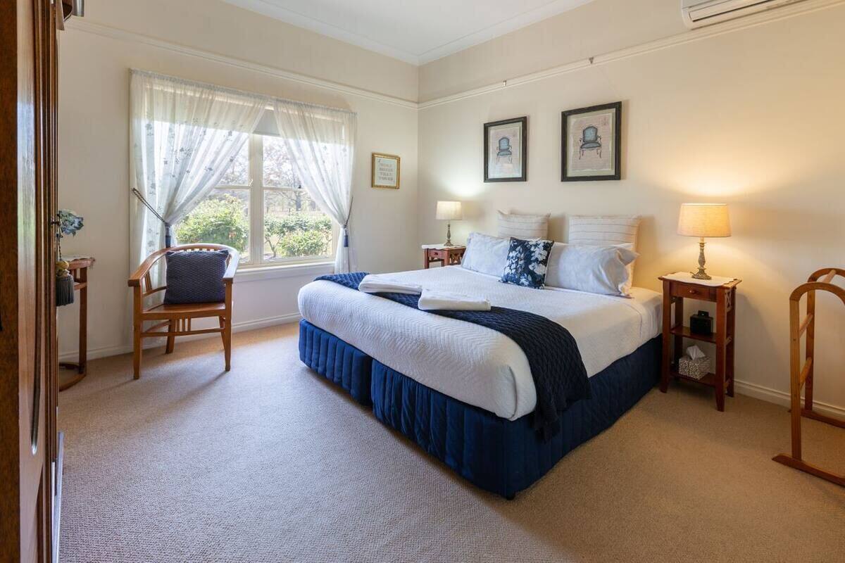 A neatly arranged bedroom with a large bed, two bedside tables, a chair, and a window with curtains.