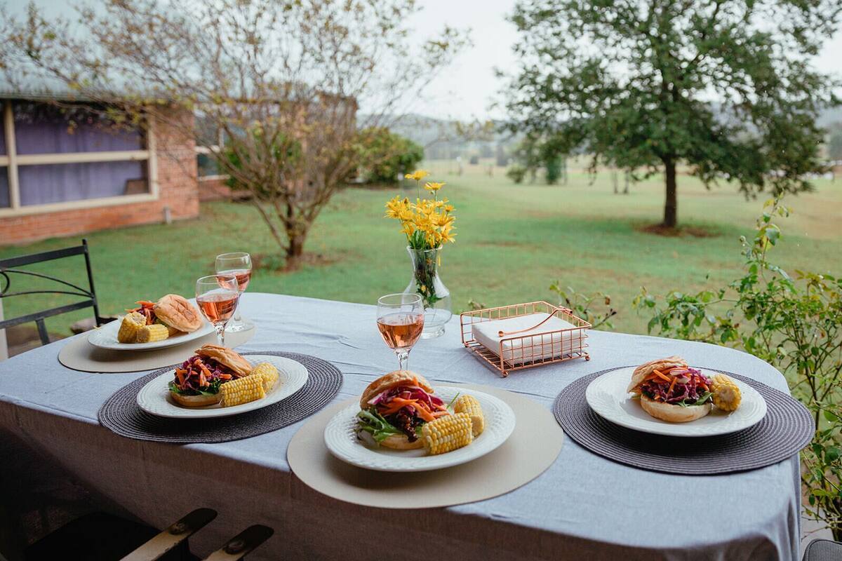 An outdoor dining table set with plates of food, glasses of wine, and a vase of flowers.
