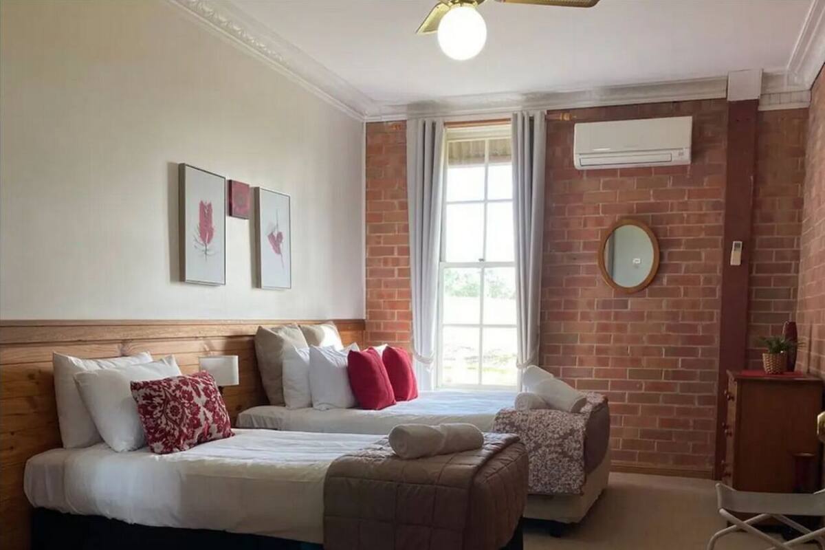 A hotel room with two beds, a wooden headboard, a brick wall, and a large window with curtains.