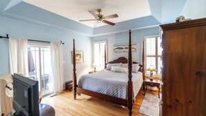 A four-poster bed with a wooden frame, a ceiling fan, and a large window with curtains. - Coastal Beauty-Bike to Beach (Lewes)