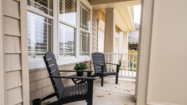A porch with two black chairs and a small table, a potted plant, and a window with shutters. - Coastal Beauty-Bike to Beach (Lewes)