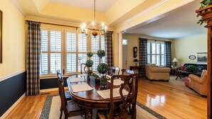 A dining area with a wooden table, chairs, and a chandelier. There is a living room in the background with a sofa and a coffee table. - Coastal Beauty-Bike to Beach (Lewes)