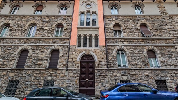 Un bâtiment en pierre avec une entrée centrale, de nombreuses fenêtres et une voiture garée devant.