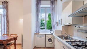 Une cuisine compacte équipée d’un lave-linge, d’une cuisinière et d ’une fenêtre avec des rideaux.