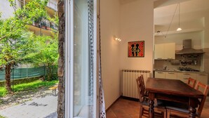 Un coin repas avec une table et des chaises, une cuisine en arrière-plan et une vue sur un balcon agrémenté de verdure.