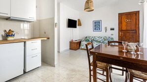A kitchen with white cabinets, a wooden countertop, and a dining area with a table and chairs. - GuestHost - Carloforte Cozy Apartment with Balcony (Carloforte)