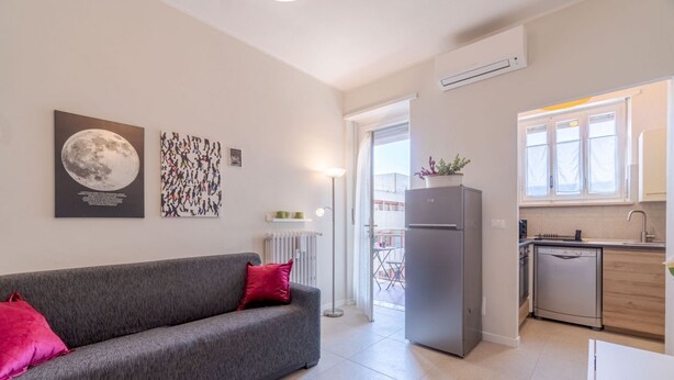 Un apartamento moderno con un sofá gris, un refrigerador, una cocina y un balcón.