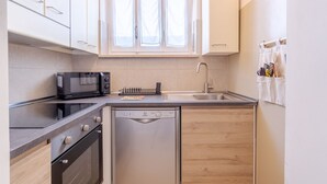 Una cocina compacta equipada con microondas, horno, lavavajillas y una ventana sobre el fregadero.