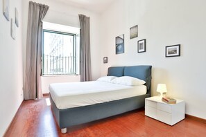 Een slaapkamer met een bed, een nachtkastje, een raam met gordijnen en wanddecoraties.