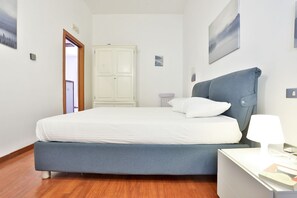 Ein Schlafzimmer mit Bett, Nachttisch, Lampe und einer Tür zu einem weiteren Raum.