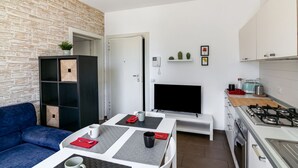 Un espacio habitable funcional con sofá, una mesa de comedor con sillas, una zona de cocina con estufa y un televisor montado en la pared.