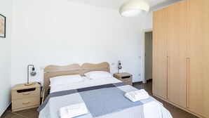 Un dormitorio con cama, mesitas de noche, un armario y una lámpara colgante.