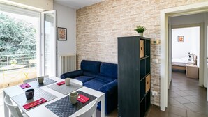 Una habitación moderna con pared de piedra, un sofá azul, una mesa de comedor con sillas y una pequeña cocina americana.