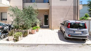 Un edificio con entrada pavimentada, un coche aparcado y una motocicleta.