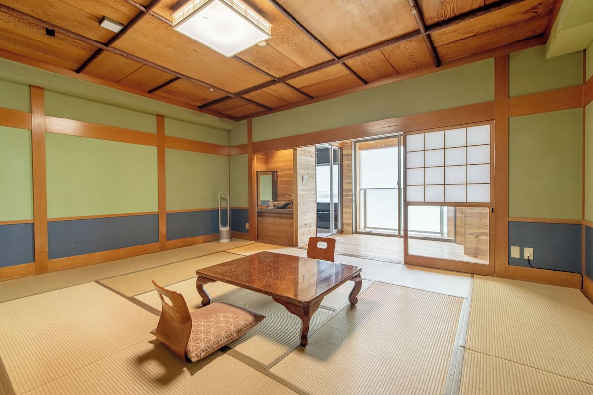 A traditional tatami room with a wooden table and chairs, a sliding door, and a view of the outside.