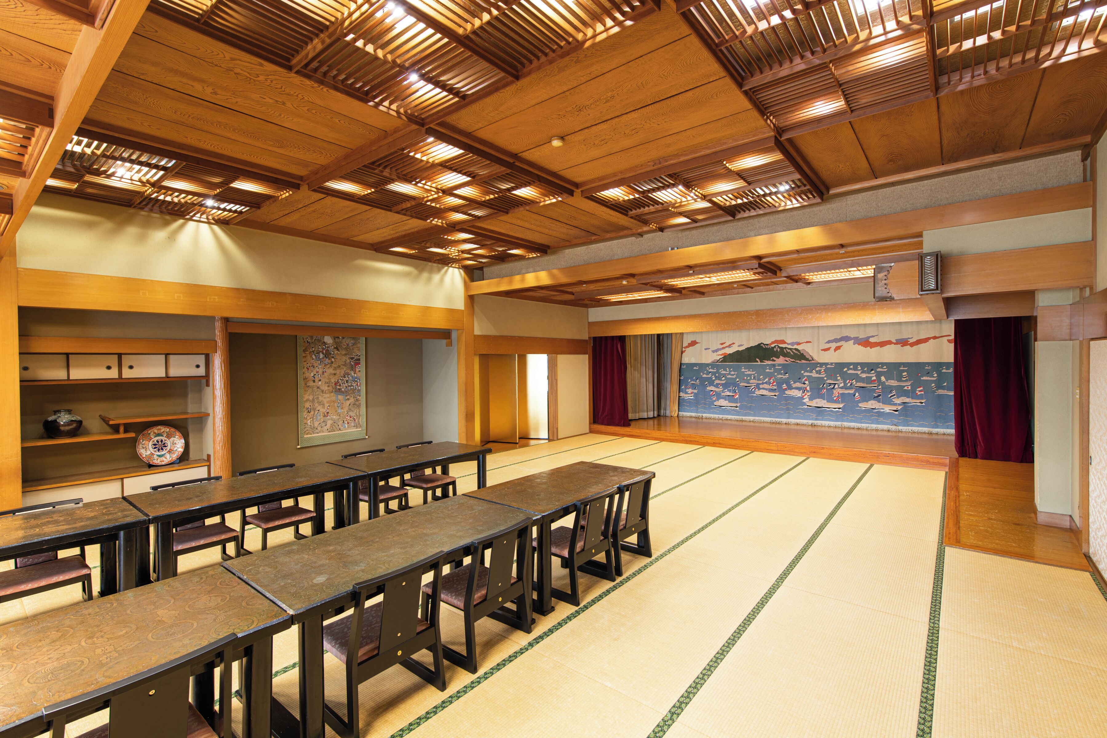 A traditional Japanese room with tatami flooring, wooden tables, and a large mural on the wall.