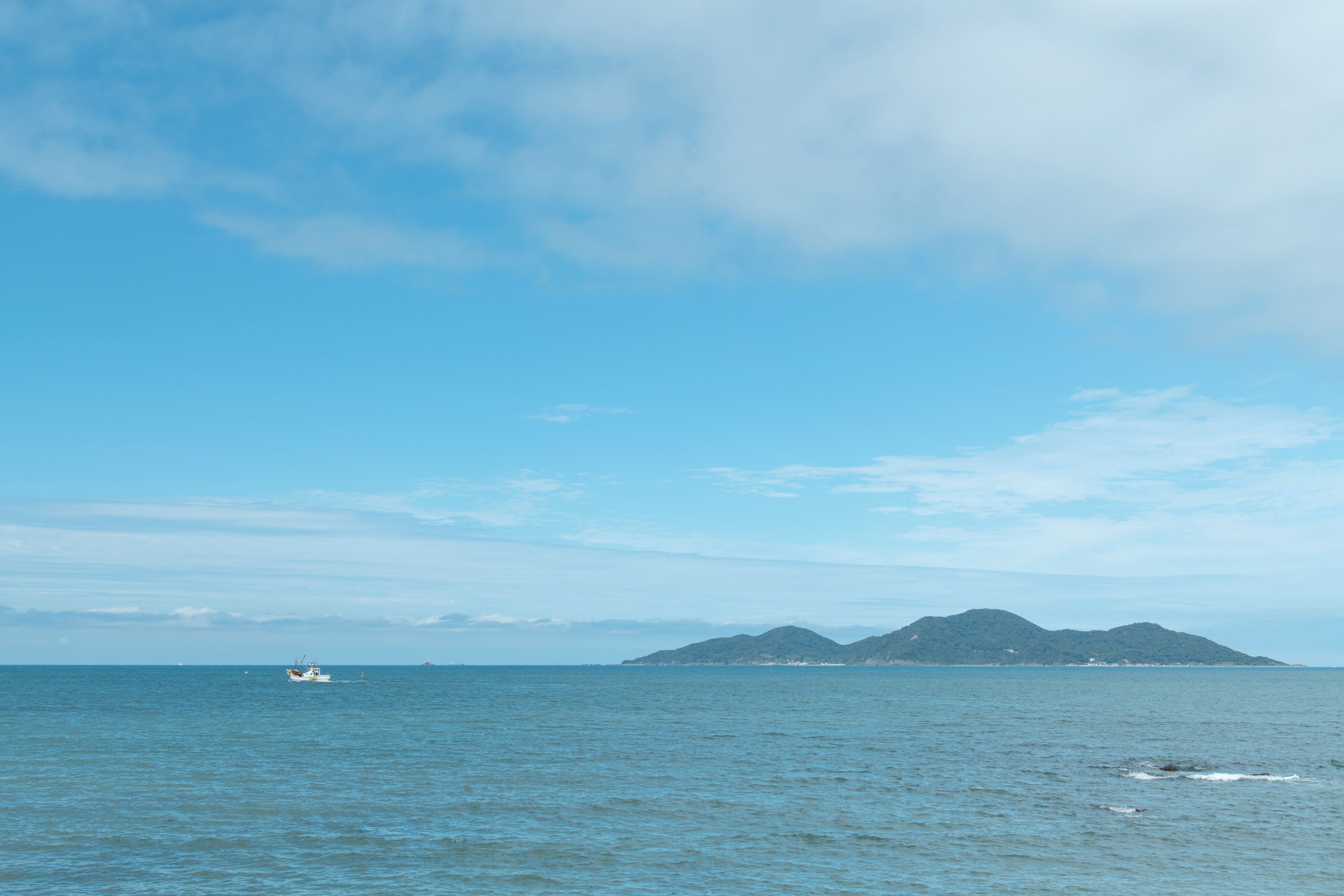 A calm sea with a boat and distant mountains under a clear sky.