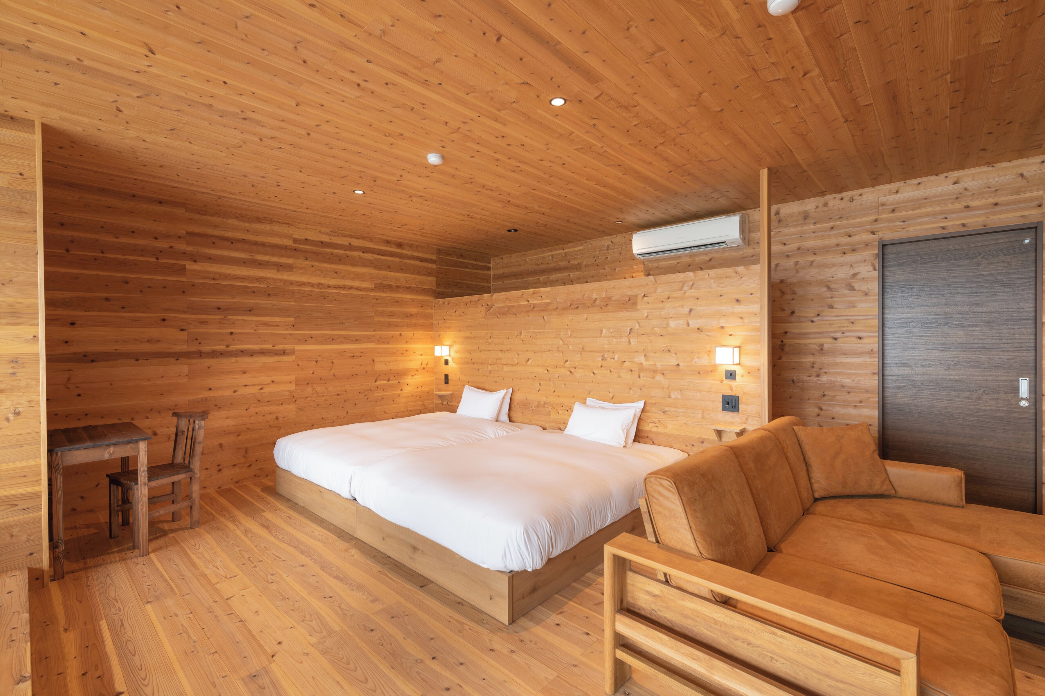 Ein Zimmer mit Holzwänden, einem großen Bett, einer Couch, einem Schreibtisch und einem Stuhl.