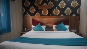 A hotel room with a large bed, a wooden headboard, and patterned wallpaper. - Hotel Rudreshwar (Haridwar)
