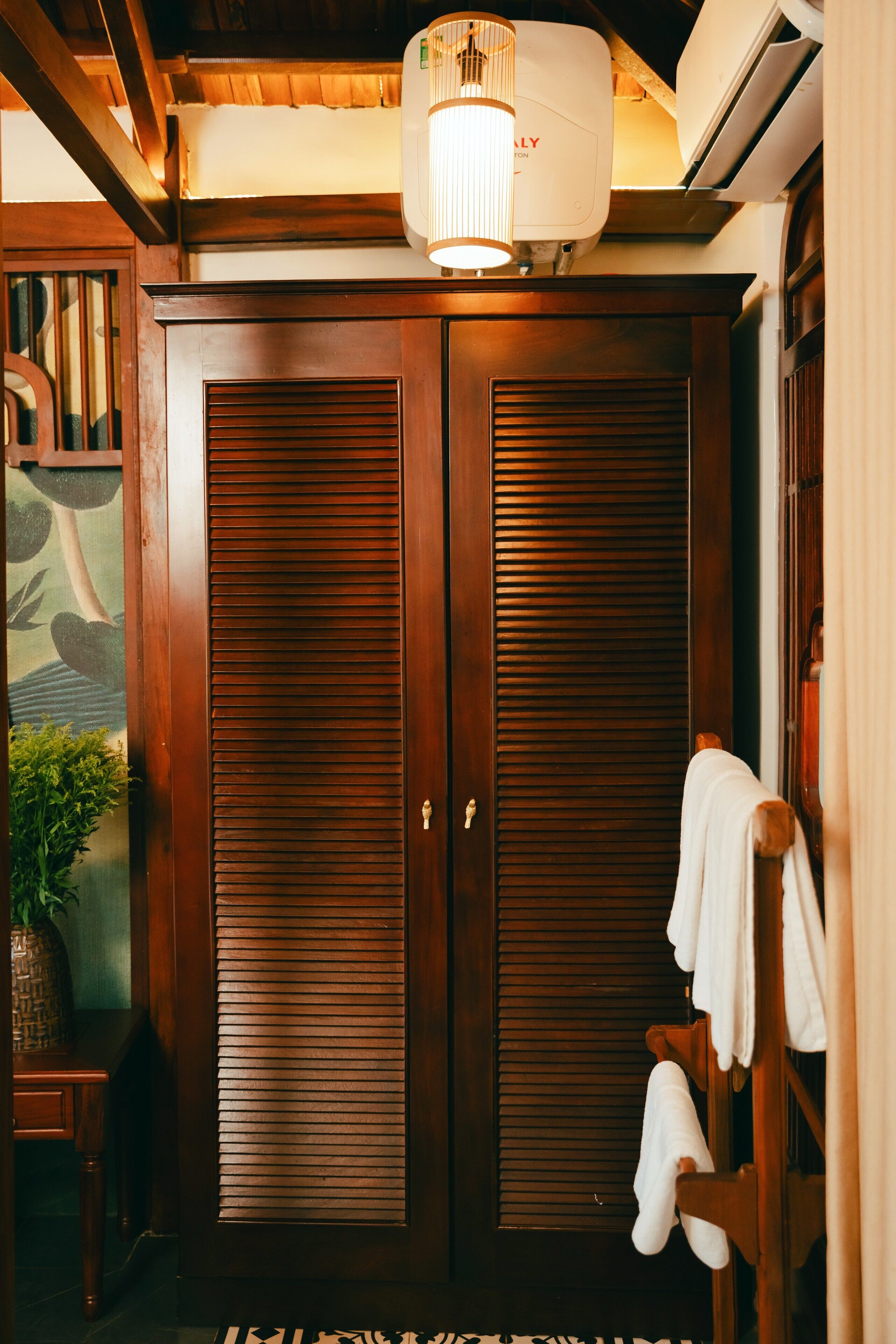 A wooden wardrobe with a sliding door, a hanging towel rack, and a potted plant.