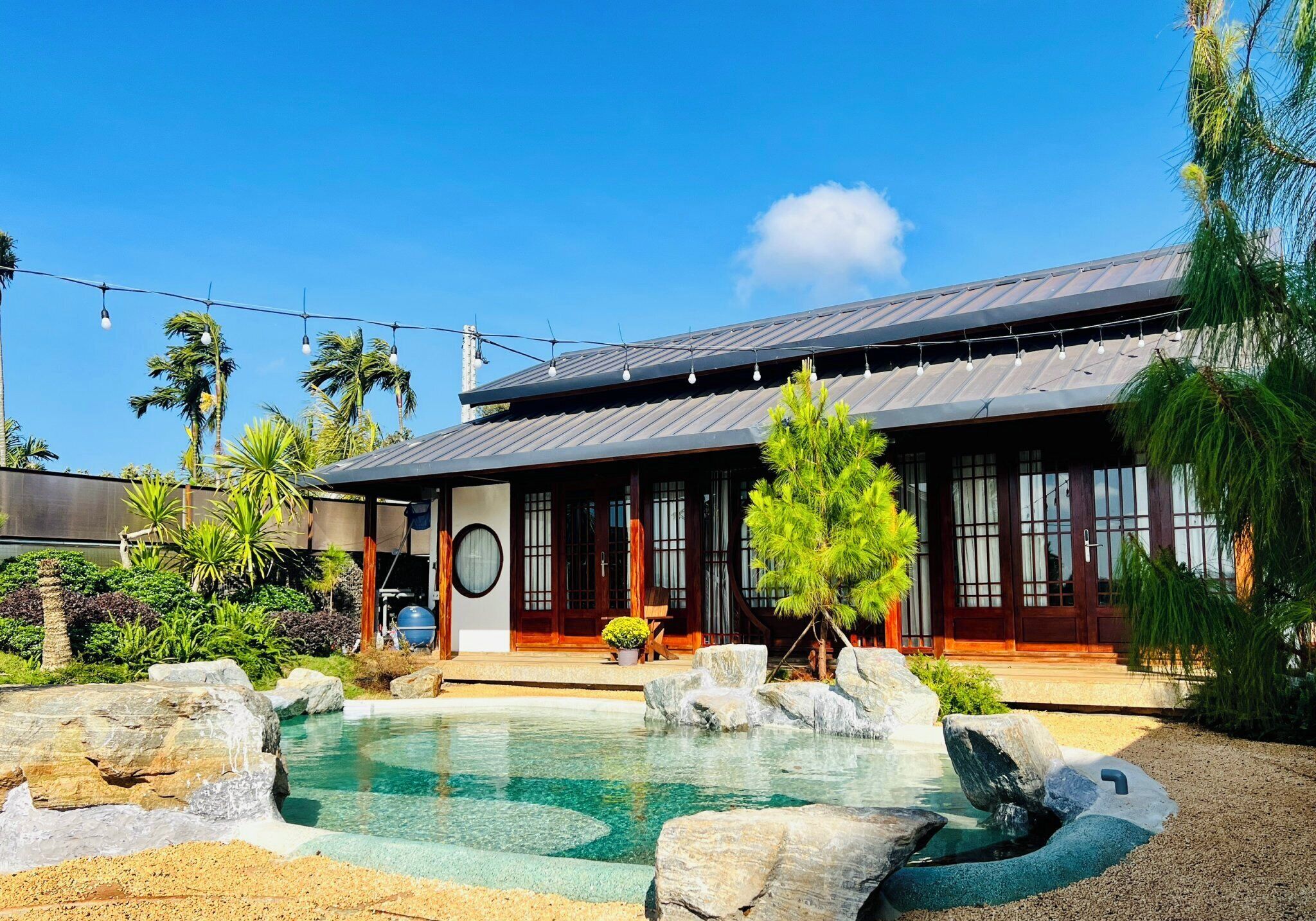 Una casa moderna con piscina, immersa nel verde di piante tropicali e un cielo azzurro limpido.