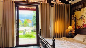 Camera d'albergo con un letto, tende, una lampada e vista sul giardino.