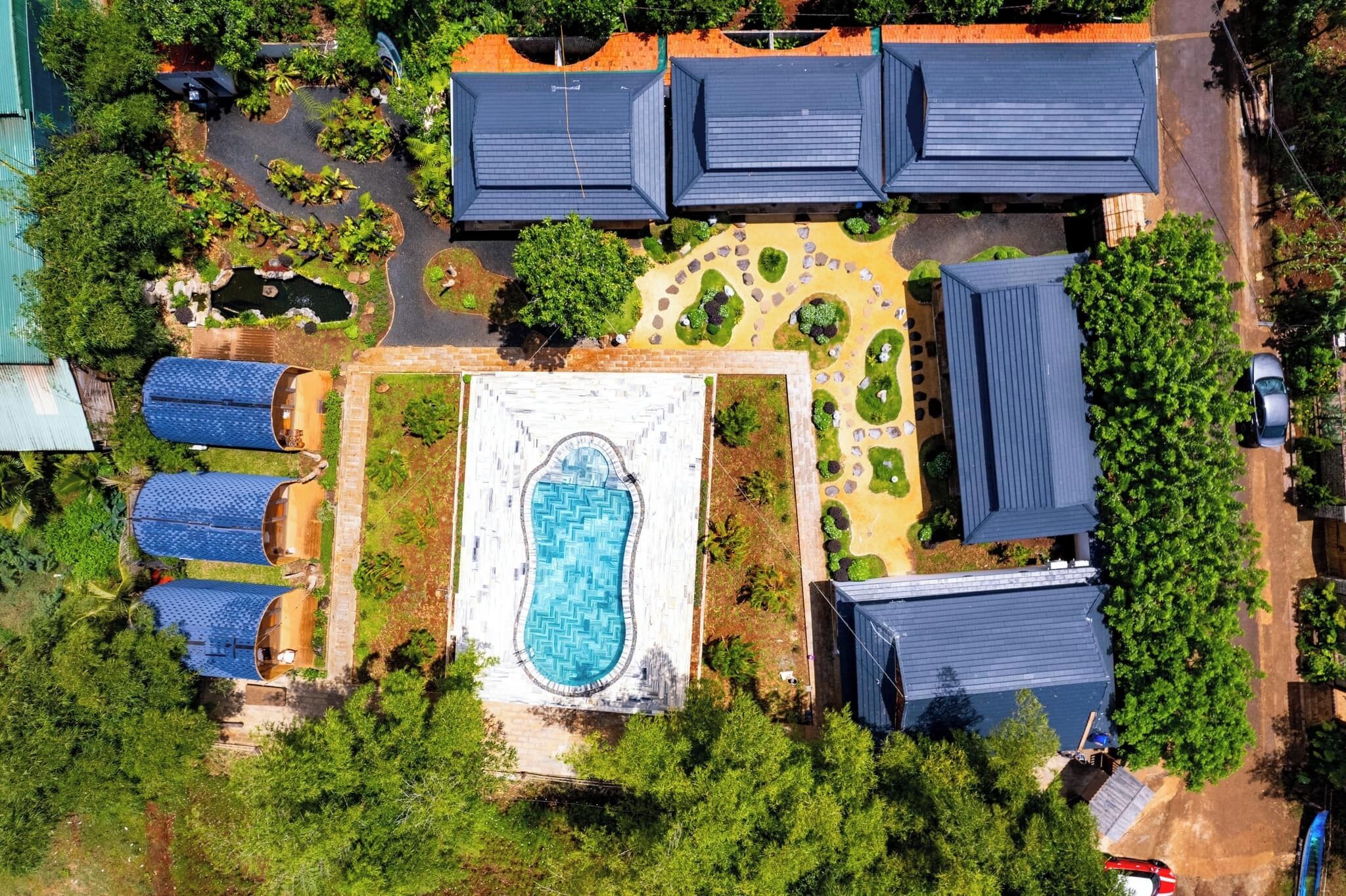 An aerial view of a resort with multiple buildings, a central swimming pool, and surrounding greenery.